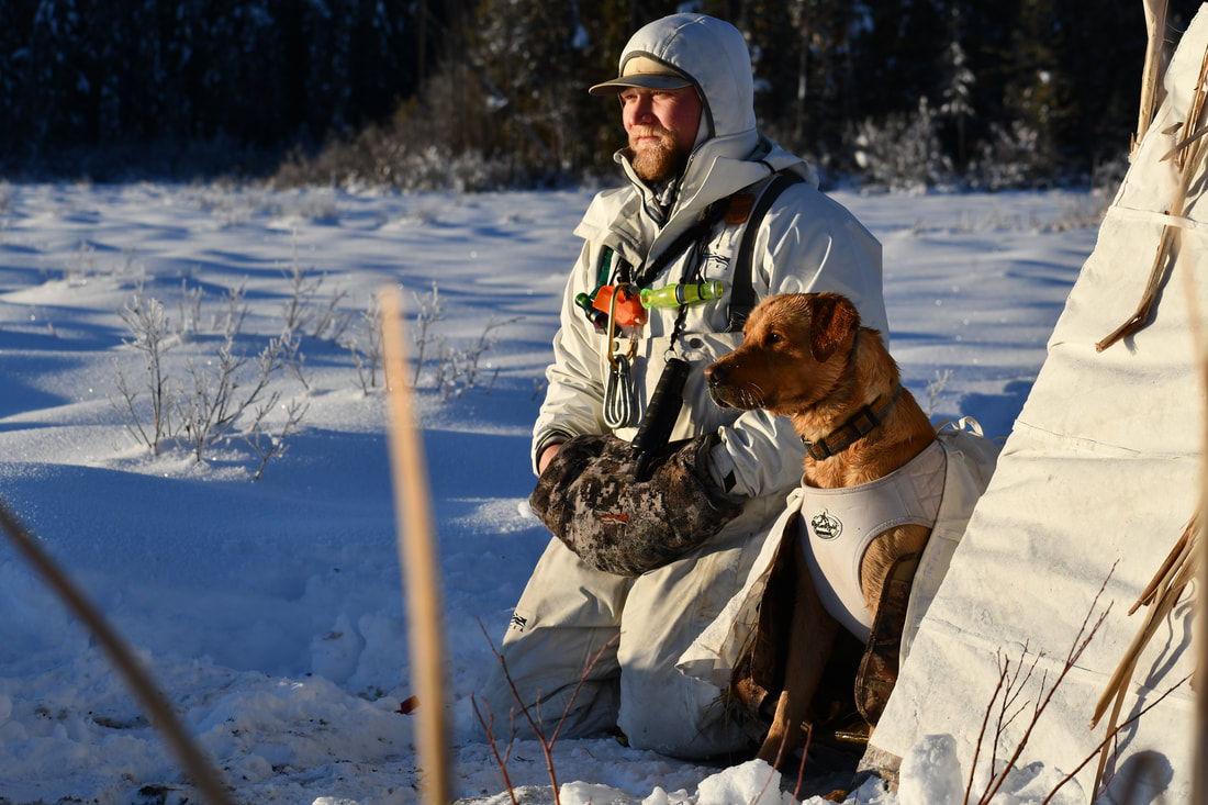 Orlyn Fenn kneeling in the snow with a hunting dog